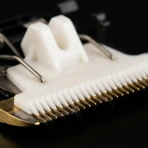 Close-up macro view of a professional dog grooming clipper blade featuring a white ceramic moving blade and a gold titanium fixed blade.