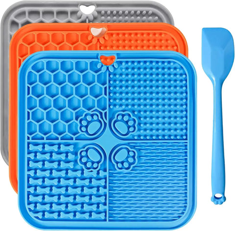 Three pack dog licking mats stacked in grey, orange, and blue colors next to a blue silicone spatula tool.