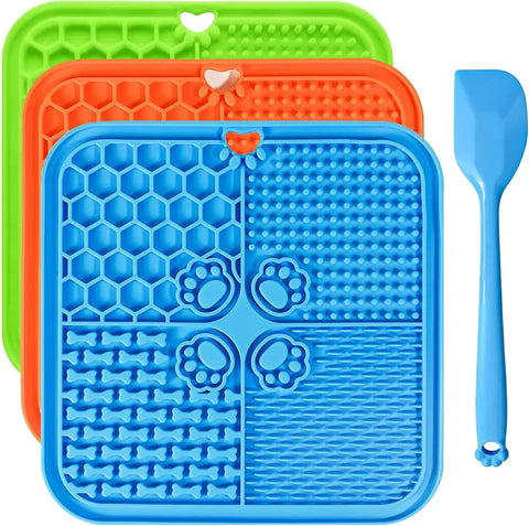 Stacked set of green, orange, and blue silicone dog licking mats designed for anxiety relief and slow feeding, with a blue spatula.
