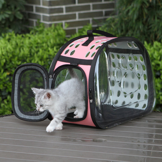 Pink pet carrier with a kitten on a wooden surface outdoors.
