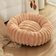 A soft beige PawVortex round pet bed with cozy plush filling and decorative ribbed texture, creating a warm and versatile circular nesting spot for dogs and cats on a wooden floor.

