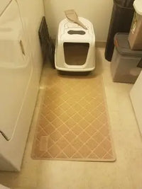 Beige mesh cat litter trapping mat placed on laundry room floor under hooded litter box with scoop