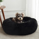 Small Schnauzer sitting upright inside a black plush calming donut dog bed