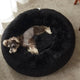 Overhead top view of a small dog sleeping peacefully inside a black plush round donut bed