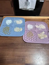 Two quadrant-style silicone pet lick mats, one light blue and one lavender purple, spread with various purees and pumpkin toppings, displayed side-by-side on a wooden countertop.