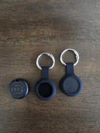 A SeekTag pet tracker shown alongside two black silicone protective sleeves with metal keychain rings.