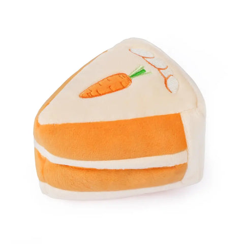 Triangular slice of plush carrot cake dog toy with orange frosting layers and embroidered carrot detail.