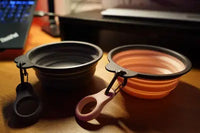 Customer photo showing gray and pink collapsible silicone dog bowls sitting on a wooden desk
