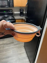 Hand holding an expanded pink collapsible silicone travel bowl in a kitchen setting customer photo