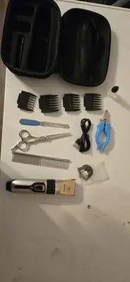 A flat lay unboxing photo of a pet grooming set including a silver and gold cordless clipper, four guard combs, grooming scissors, a metal comb, a nail file, and blue nail trimmers.