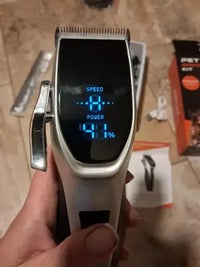 Close-up of cordless pet grooming clippers showing the digital LED battery power indicator and speed settings screen.