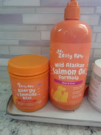A customer's review image displaying a tub of Zesty Paws Allergy and Immune Bites next to a large pump bottle of Wild Alaskan Salmon Oil Formula on a bathroom counter.