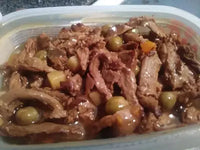 A close-up view of wet dog food featuring meat chunks, gravy, green peas, and diced carrots.