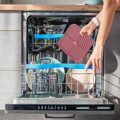 A person loading a flexible pink silicone dog lick mat directly into a kitchen dishwasher for easy cleaning.