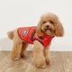 Dog wearing a red jacket with  a light wooden floor.