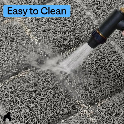 Close-up of water hose rinsing litter debris off a gray mesh cat litter trapping mat