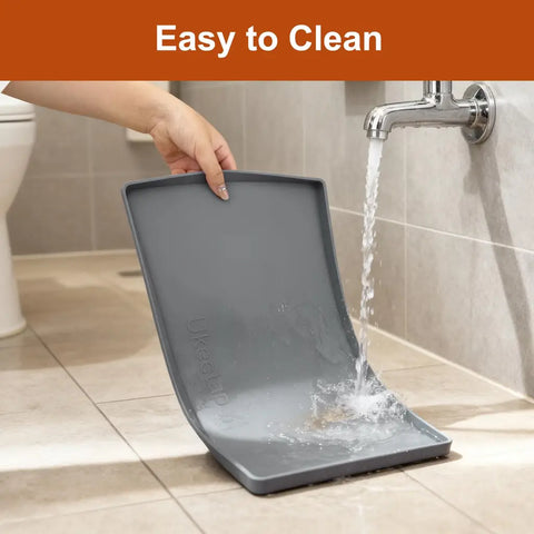 A person rinsing a flexible grey silicone pet placemat under running tap water in a bathroom to show how easy it is to clean.