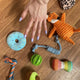  Flat lay of various plush and rope dog toys including a blue donut and green avocado on a hardwood floor next to a customer's hand, customer review image.