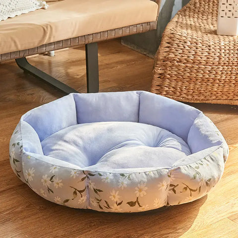 Floral-patterned pet bed on wooden floor with couch in background.