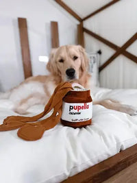 Real customer photo of a Golden Retriever resting on a bed with the Pupella chocolate hazelnut spread plush dog puzzle toy.