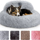 Medium dog lying in a light gray plush round donut bed with head support