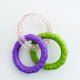 Interlocking green, purple, and clear glitter rubber chew rings for dogs on a white background