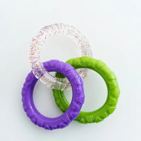 Interlocking green, purple, and clear glitter rubber chew rings for dogs on a white background
