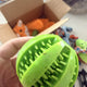 Customer hand holding a green rubber studded chew ball dog toy with a box of plush pet toys in the background, customer review image.