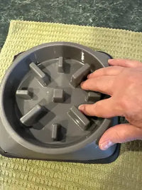A person's hand inside a grey plastic slow feeder dog bowl to show the depth and size of the feeding ridges.