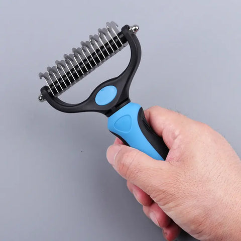 Hand holding pet grooming tool with blue handle and black bristle side.