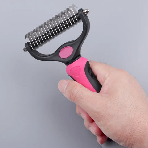 Hand holding pink and black pet grooming tool against gray background.