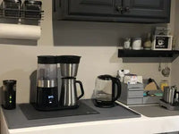 Gray silicone kitchen appliance mat placed under a coffee maker and electric kettle to protect the white countertop from spills and heat.
