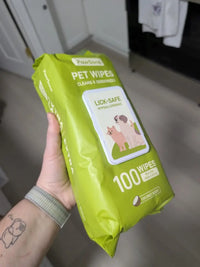 Customer with wristband and arm tattoo holding up full green package of PawSono coconut scented pet wipes indoors