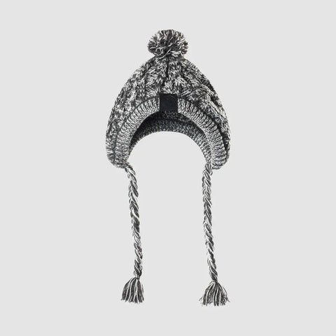 Knitted beanie with pom-pom and tassels on light gray background.