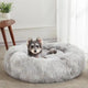 Small terrier sitting comfortably inside a light grey plush round donut dog bed