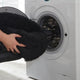Hands loading a washable black plush donut dog bed into a front-load washing machine