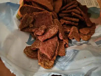 Close-up view of the rough, natural texture of dried jerky dog treats inside the packaging.
