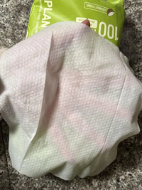 Close-up customer review showing thick texture of white PawSono plant-based pet wipe held over hand with green packaging in background