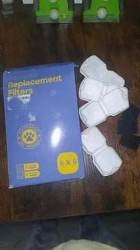 Black porous replacement pre-filter sponges for a stainless steel automatic pet water fountain pump displayed on a white marble counter.