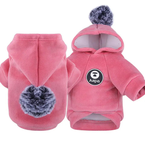 Pink dog hoodie with pom-poms on white background.