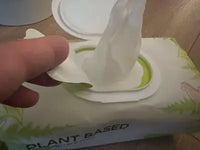 A customer's hand pulling a moist, plant-based pet glove wipe out of the plastic flip-top packaging dispenser.
