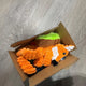 Orange plush fox and green avocado dog toys packed inside a small open shipping box on a grey floor, customer review image.