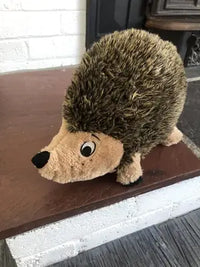 close up side view of brown and tan stuffed plush hedgehog dog toy on fireplace hearth