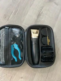 An open pet grooming kit featuring a black electric clipper, blue handle dog nail trimmers, and black plastic guard combs in a structured case.