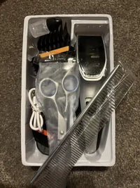 Overhead view of a dog grooming kit in its packaging box showing clippers, a stainless steel comb, grooming shears, and oil.