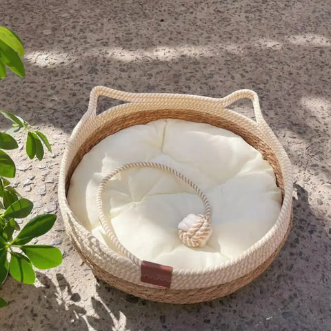 Round woven pet bed with white cushion on concrete surface.