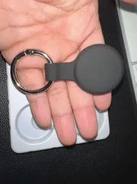 A matte black silicone protective case for a pet tracker with a silver carabiner ring held in a person's palm.