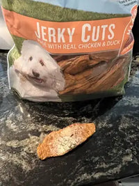 A single piece of Nudges Jerky Cut dog treat placed on a dark countertop next to the product bag.