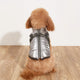 Small dog wearing a silver reflective jacket on wooden floor.