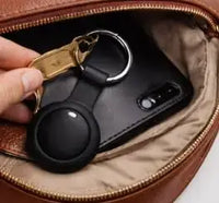 A black smart tag tracker attached to keys being placed inside a brown leather handbag for pet or personal item tracking.
